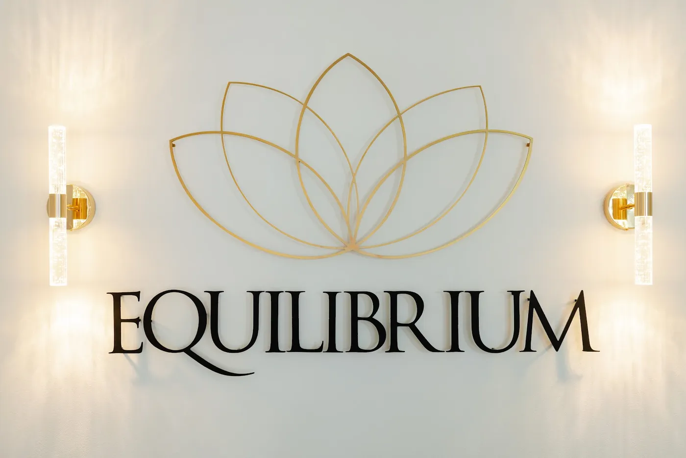 Letreiro Equilibrium com a flor de lótus dourada entre duas arandelas, na parede da clínica